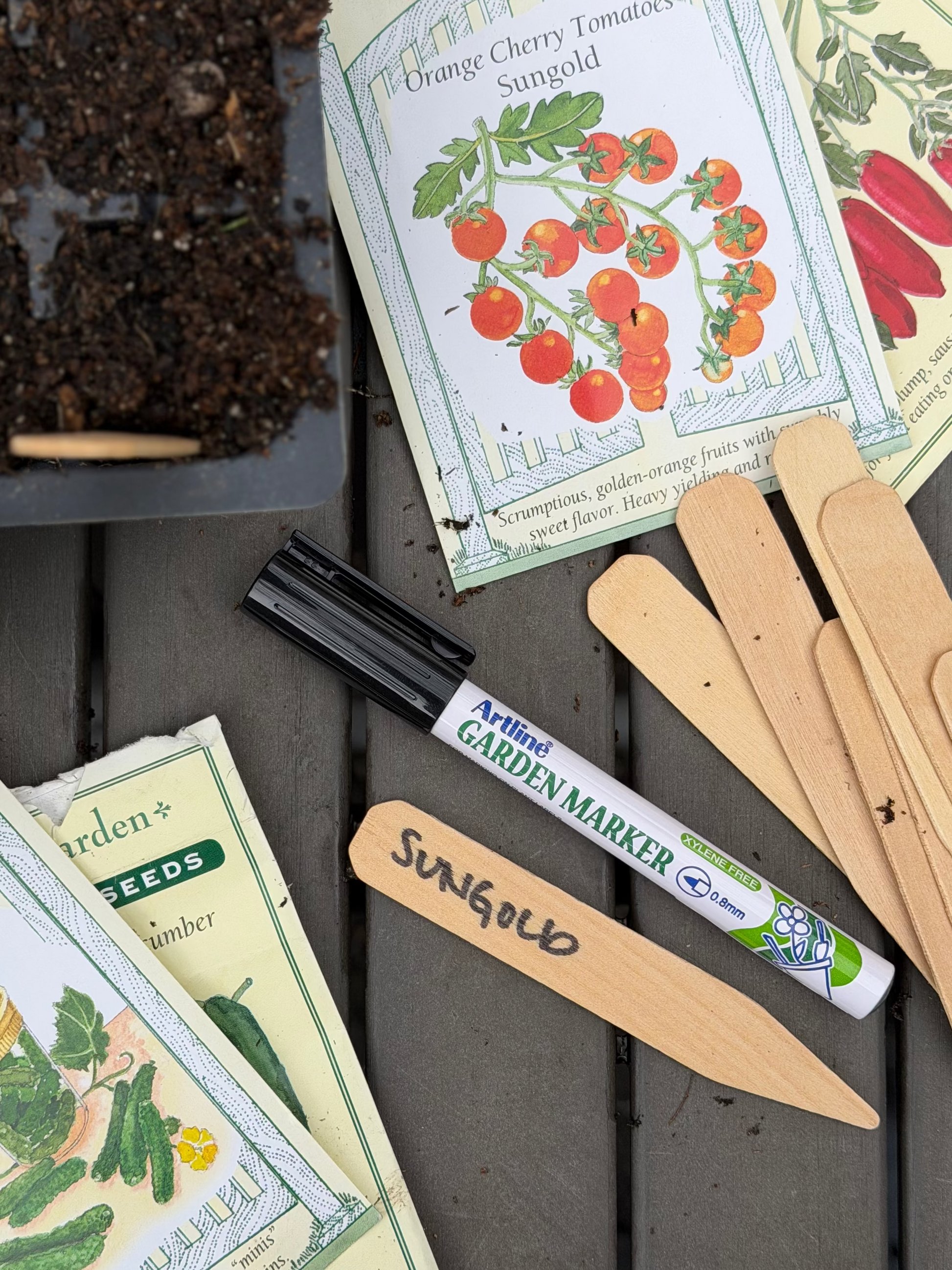 Seed packets, garden markers, and a trowel on a wooden surface