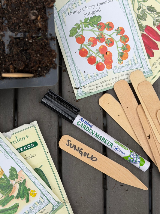 Seed packets, garden markers, and a trowel on a wooden surface